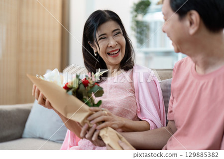 Joyful Senior Couple Celebrating Valentine's Day with Flowers and Smiles in a Cozy Home Setting 129885382