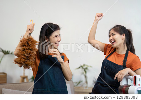 Joyful Women Engaged in House Cleaning with Feather Duster and Vacuum in Modern Living Room Setting Joyful Women Engaged in House Cleaning with Feather Duster and Vacuum in Modern Living Room Setting 129885398