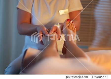Foot Massage Therapy in a Relaxing Spa Setting. A professional massage therapist in a white uniform provides a soothing foot massage to a client in a calm and serene spa environment Foot Massage Therapy in a Relaxing Spa Setting. A professional massage therapist in a white uniform provides a soothing foot massage to a client in a calm and serene spa environment 129885442