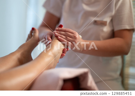 Foot Massage Therapy in a Relaxing Spa Setting. A professional massage therapist in a white uniform provides a soothing foot massage to a client in a calm and serene spa environment Foot Massage Therapy in a Relaxing Spa Setting. A professional massage therapist in a white uniform provides a soothing foot massage to a client in a calm and serene spa environment 129885451