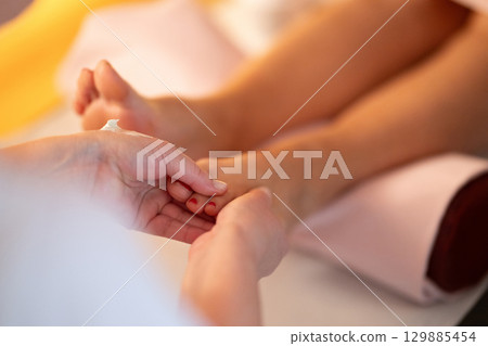 Foot Massage Therapy in a Relaxing Spa Setting. A professional massage therapist in a white uniform provides a soothing foot massage to a client in a calm and serene spa environment Foot Massage Therapy in a Relaxing Spa Setting. A professional massage therapist in a white uniform provides a soothing foot massage to a client in a calm and serene spa environment 129885454