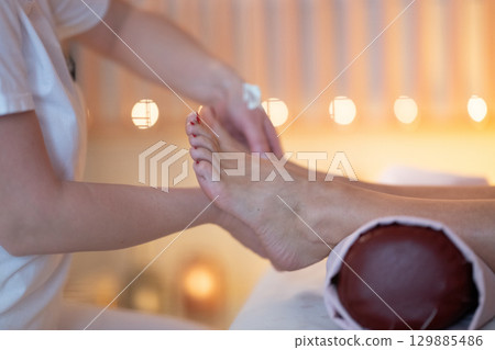 Foot Massage Therapy in a Relaxing Spa Setting. A professional massage therapist in a white uniform provides a soothing foot massage to a client in a calm and serene spa environment Foot Massage Therapy in a Relaxing Spa Setting. A professional massage therapist in a white uniform provides a soothing foot massage to a client in a calm and serene spa environment 129885486