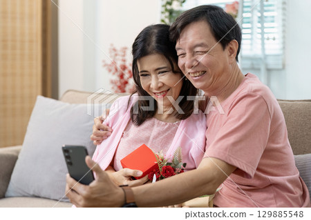 Happy Senior Couple Celebrating Valentine's Day with Gifts and Smiles in a Cozy Home Setting 129885548