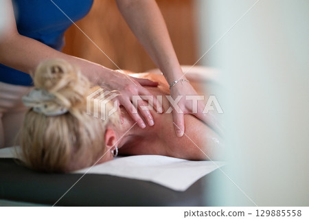 Relaxing Back Massage in a Spa Setting. A professional massage therapist in a blue uniform provides a relaxing back massage to a client lying on a massage table. Relaxing Back Massage in a Spa Setting. A professional massage therapist in a blue uniform provides a relaxing back massage to a client lying on a massage table. 129885558