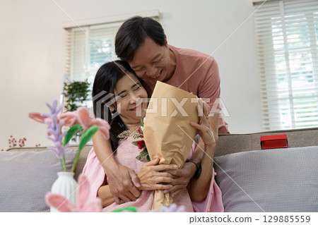 Romantic Valentine's Day Celebration with Happy Couple Embracing and Sharing a Bouquet of Flowers in Cozy Home Setting Romantic Valentine's Day Celebration with Happy Couple Embracing and Sharing a Bouquet of Flowers in Cozy Home Setting 129885559