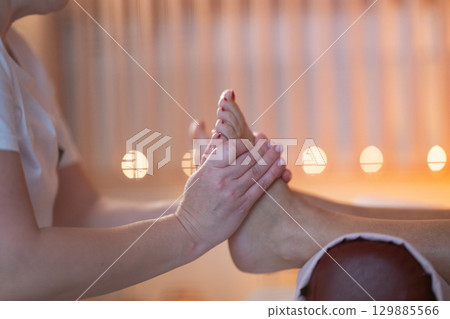 Foot Massage Therapy in a Relaxing Spa Setting. A professional massage therapist in a white uniform provides a soothing foot massage to a client in a calm and serene spa environment 129885566