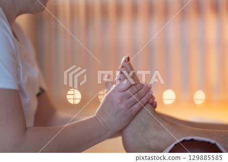 Foot Massage Therapy in a Relaxing Spa Setting. A professional massage therapist in a white uniform provides a soothing foot massage to a client in a calm and serene spa environment Foot Massage Therapy in a Relaxing Spa Setting. A professional massage therapist in a white uniform provides a soothing foot massage to a client in a calm and serene spa environment 129885585