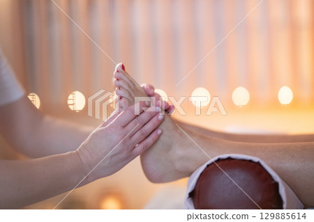 Foot Massage Therapy in a Relaxing Spa Setting. A professional massage therapist in a white uniform provides a soothing foot massage to a client in a calm and serene spa environment Foot Massage Therapy in a Relaxing Spa Setting. A professional massage therapist in a white uniform provides a soothing foot massage to a client in a calm and serene spa environment 129885614