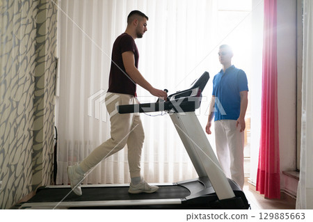 Physical Therapy on Treadmill.Man undergoing physical therapy with trainer assistance on a treadmill indoors. 129885663