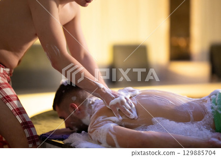 Back Massage with Foam.Therapist applying soap foam with hands on patient back during traditional bath ritual. Back Massage with Foam.Therapist applying soap foam with hands on patient back during traditional bath ritual. 129885704