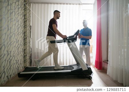 Physical Therapy on Treadmill.Man undergoing physical therapy with trainer assistance on a treadmill indoors. Physical Therapy on Treadmill.Man undergoing physical therapy with trainer assistance on a treadmill indoors. 129885711