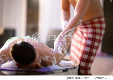 Hand Foam Therapy. Attendant gently washing patient hands with foamy soap in traditional bath setting. 129885729