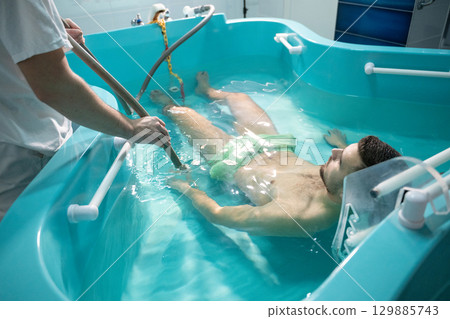 Therapeutic Water Bath.Man relaxing in hydrotherapy bath while therapist adjusts water settings. 129885743
