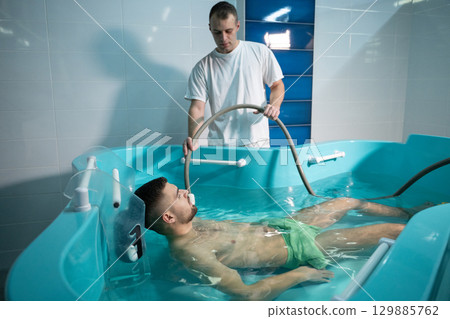 Therapeutic Water Bath.Man relaxing in hydrotherapy bath while therapist adjusts water settings. 129885762