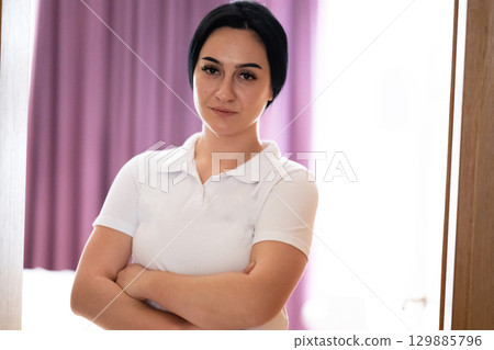 Portrait of a confident young female healthcare worker in a white uniform standing with arms crossed. 129885796