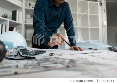 Engineer Analyzing Architectural Blueprints in Modern Office Setting with Tools and Safety Gear 129885934