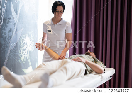 A female therapist performs a arm stretch technique on a male patient lying on a treatment bed. A female therapist performs a arm stretch technique on a male patient lying on a treatment bed. 129885977
