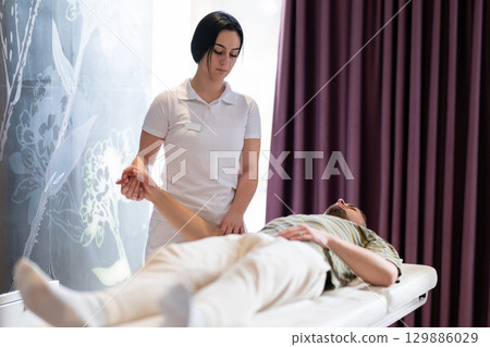 A female therapist performs a arm stretch technique on a male patient lying on a treatment bed. A female therapist performs a arm stretch technique on a male patient lying on a treatment bed. 129886029