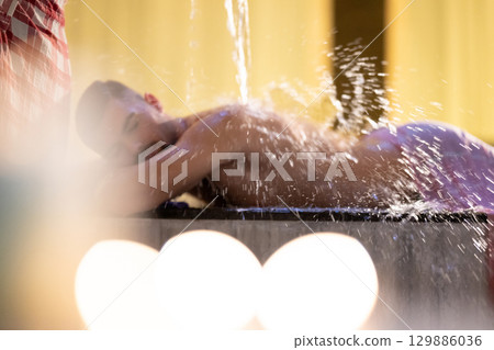 Man receiving water therapy inside a traditional Turkish hammam with ornate details. Man receiving water therapy inside a traditional Turkish hammam with ornate details. 129886036