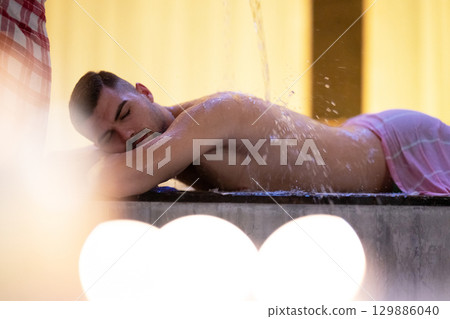 Man receiving water therapy inside a traditional Turkish hammam with ornate details. 129886040