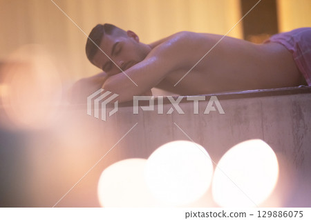 Man relaxing on a marble platform inside a Turkish bath with warm lighting. Man relaxing on a marble platform inside a Turkish bath with warm lighting. 129886075