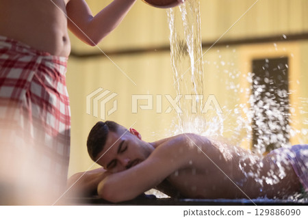 Man receiving water therapy inside a traditional Turkish hammam with ornate details. Man receiving water therapy inside a traditional Turkish hammam with ornate details. 129886090