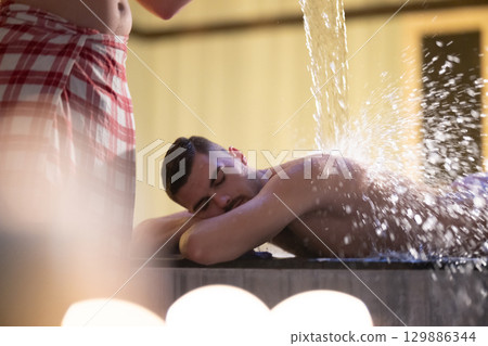 Man receiving water therapy inside a traditional Turkish hammam with ornate details. Man receiving water therapy inside a traditional Turkish hammam with ornate details. 129886344