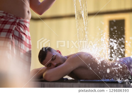 Man receiving water therapy inside a traditional Turkish hammam with ornate details. Man receiving water therapy inside a traditional Turkish hammam with ornate details. 129886393