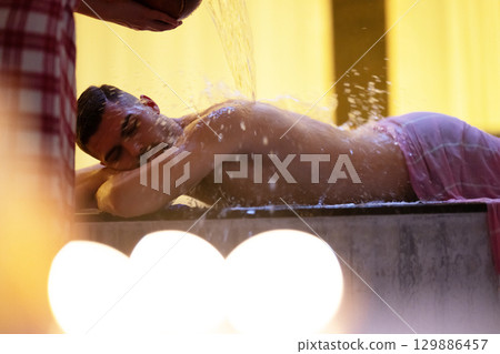 Man receiving water therapy inside a traditional Turkish hammam with ornate details. Man receiving water therapy inside a traditional Turkish hammam with ornate details. 129886457