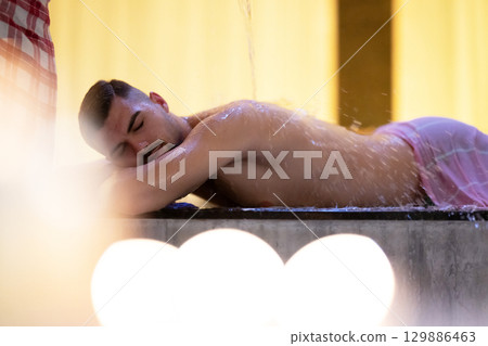 Man receiving water therapy inside a traditional Turkish hammam with ornate details. Man receiving water therapy inside a traditional Turkish hammam with ornate details. 129886463