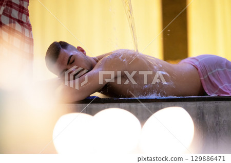 Man receiving water therapy inside a traditional Turkish hammam with ornate details. Man receiving water therapy inside a traditional Turkish hammam with ornate details. 129886471