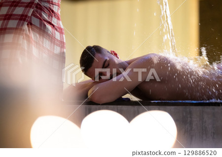Man receiving water therapy inside a traditional Turkish hammam with ornate details. 129886520