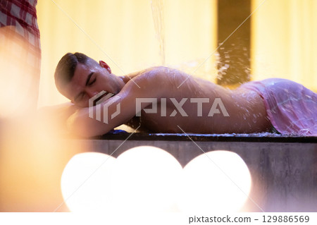 Man receiving water therapy inside a traditional Turkish hammam with ornate details. 129886569