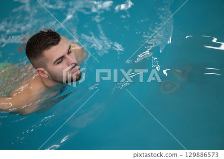 Man doing aquatic therapy or swimming exercises in a professional spa facility indoor pool. 129886573