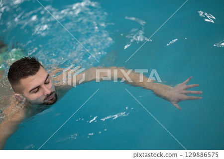 Man doing aquatic therapy or swimming exercises in a professional spa facility indoor pool. 129886575