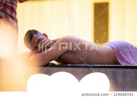 Man receiving water therapy inside a traditional Turkish hammam with ornate details. Man receiving water therapy inside a traditional Turkish hammam with ornate details. 129886591