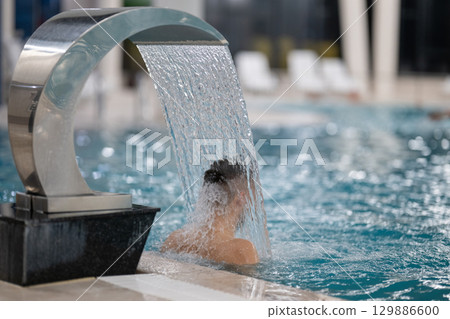 Man standing under a hydrotherapy waterfall in a spa pool, receiving water massage on his head and shoulders. Man standing under a hydrotherapy waterfall in a spa pool, receiving water massage on his head and shoulders. 129886600
