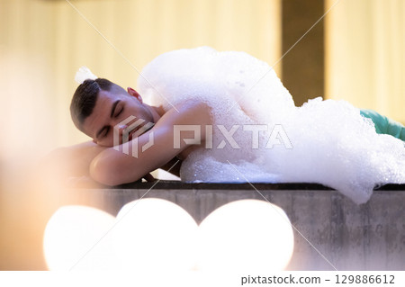 Man Relaxing in Foam.Relaxed man lying in Turkish bath covered in white foam during cleansing ritual. 129886612