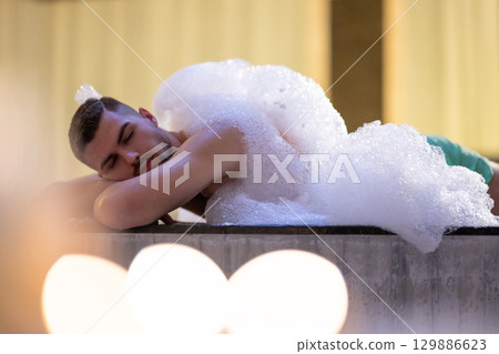 Man Relaxing in Foam.Relaxed man lying in Turkish bath covered in white foam during cleansing ritual. 129886623