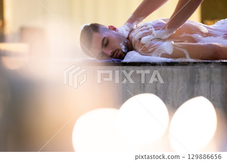 Back Massage with Foam.Therapist applying soap foam with hands on patient back during traditional bath ritual. 129886656