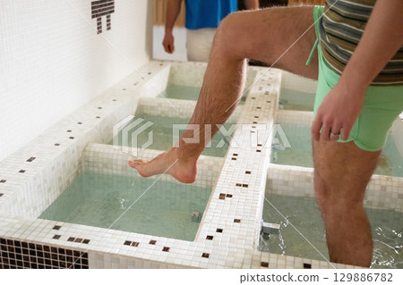 Man Stepping in Spa Water Walkway.Close up of a mans legs as he steps into tiled spa therapy pools for a hydrotherapy session. 129886782