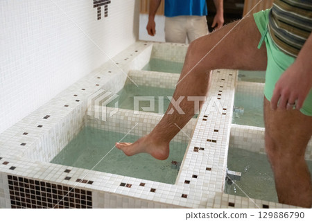 Man Stepping in Spa Water Walkway.Close up of a mans legs as he steps into tiled spa therapy pools for a hydrotherapy session. Man Stepping in Spa Water Walkway.Close up of a mans legs as he steps into tiled spa therapy pools for a hydrotherapy session. 129886790