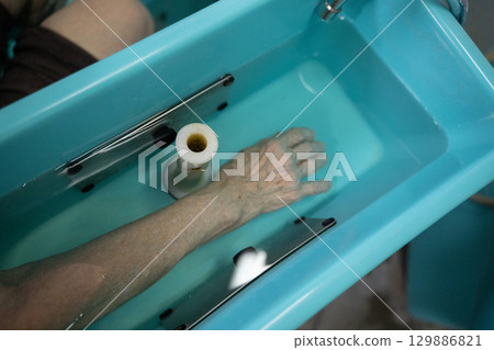 Closeup view of a senior hand submerged in water in a hydrotherapy machine for medical treatment. Closeup view of a senior hand submerged in water in a hydrotherapy machine for medical treatment. 129886821