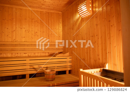 Empty Wooden Sauna Interior.Wide view of a warm and empty wooden sauna with rolled towels and wooden benches prepared for relaxation. Empty Wooden Sauna Interior.Wide view of a warm and empty wooden sauna with rolled towels and wooden benches prepared for relaxation. 129886824