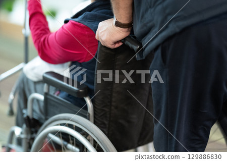 Wheelchair Assistance Close Up.Partial view of a person assisting someone in a wheelchair, showing hands and wheels. 129886830