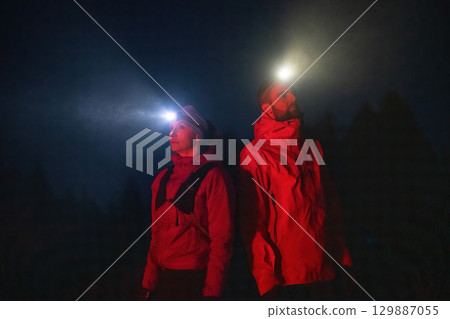 Exploring the Night Forest.Couple equipped with headlamps explore a forest in total darkness, with beams of light cutting through the night air. 129887055