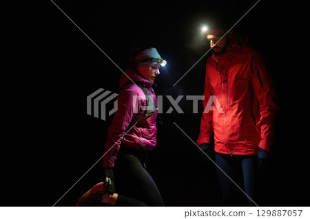Exploring the Night Forest.Couple equipped with headlamps explore a forest in total darkness, with beams of light cutting through the night air. 129887057