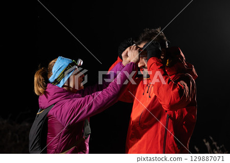Nighttime First Aid in the Wilderness.A woman provides headlamp-assisted first aid to a man outdoors in the dark, showcasing emergency preparedness in extreme conditions. 129887071