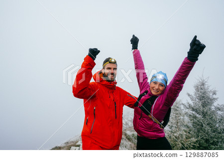 Victory Celebration at the Summit.Two hikers raise their arms in celebration at the mountain summit, showing joy and success after a long night trek. 129887085