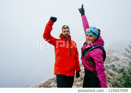Victory Celebration at the Summit.Two hikers raise their arms in celebration at the mountain summit, showing joy and success after a long night trek. 129887099